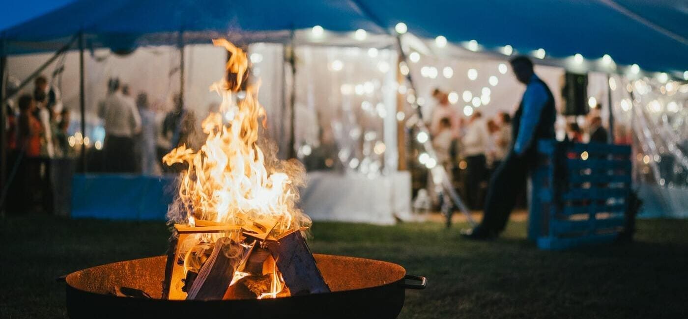 Atmospheric winter party setup with warm lighting, fire bowls and guests gathering outdoors in January