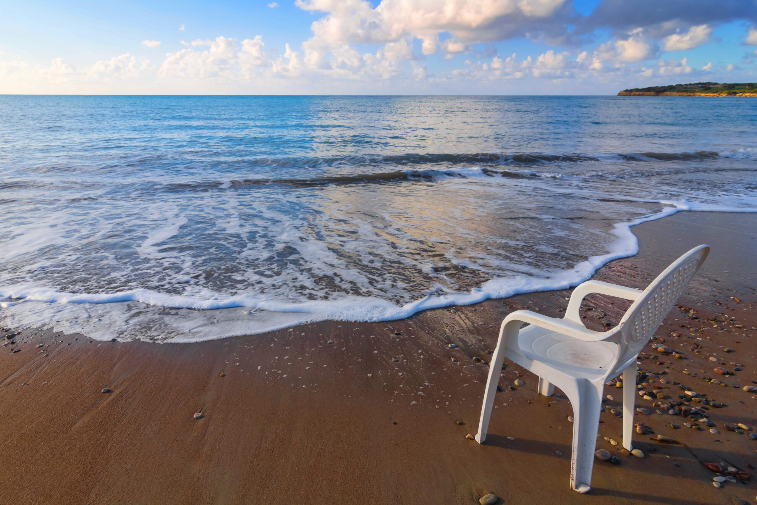 White plastic chair hire with single plastic chair on beach at tide line.