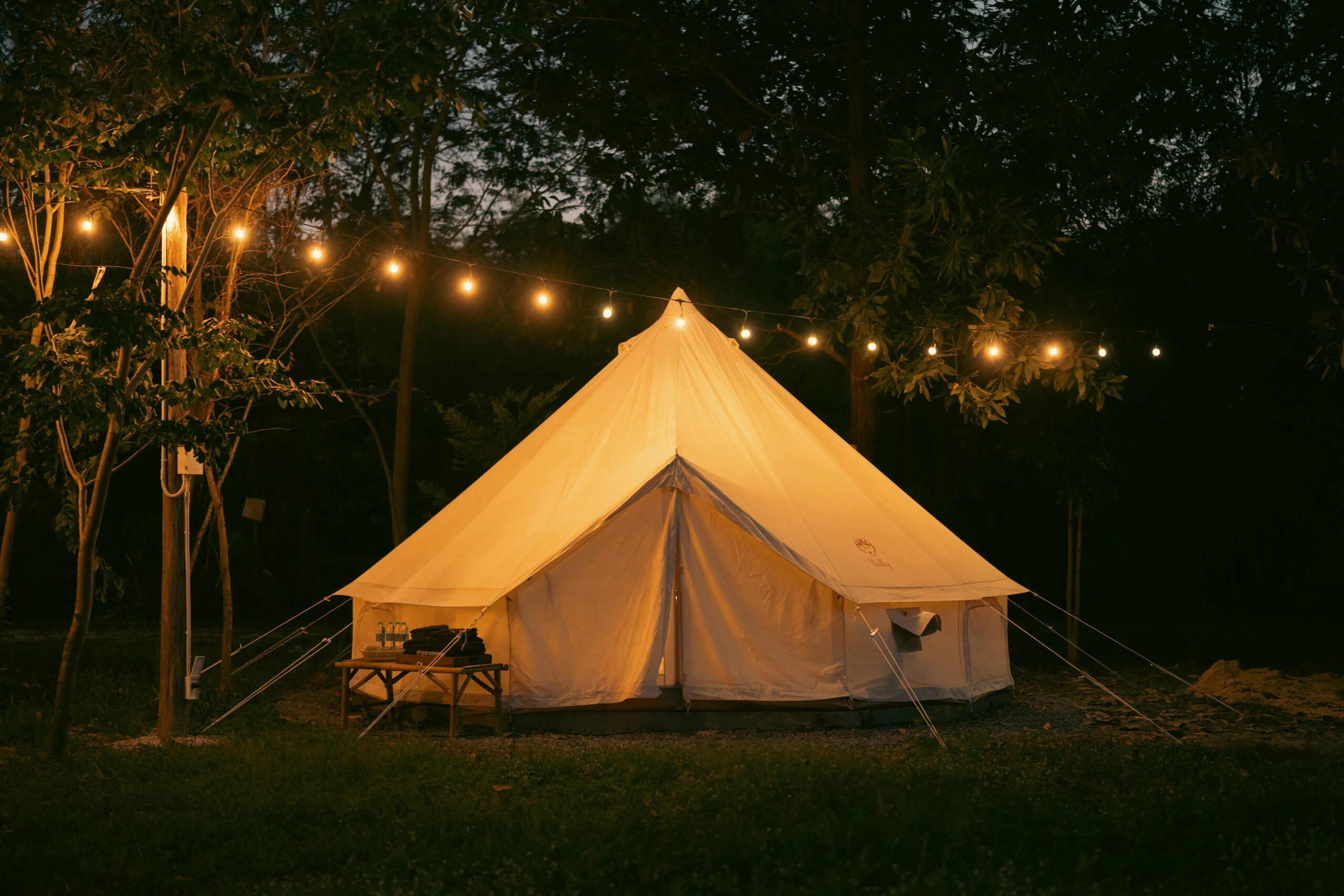 Bell tent hire in Suffolk at night, showing a cream bell tent with fairy lights in woodland clearing